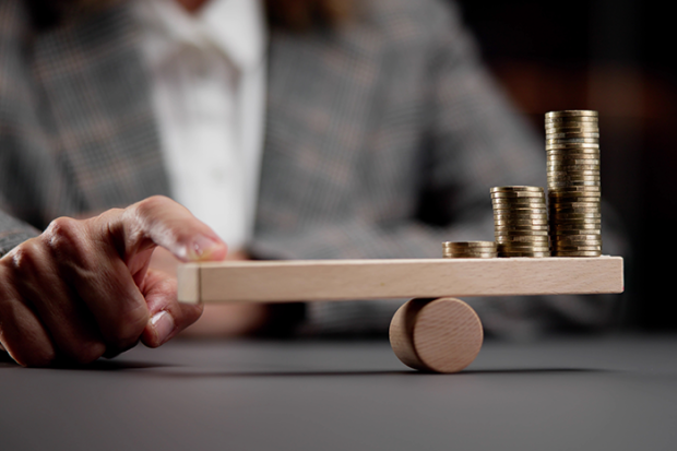 person holding finger on a fulcrum balance with coins balanced on the other side