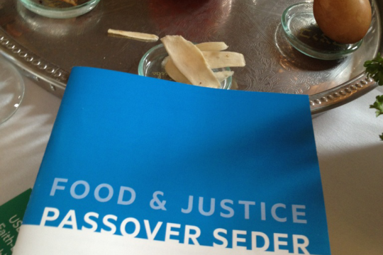 Photo of a seder plate with a book that says "Foot & Justice Passover Seder"