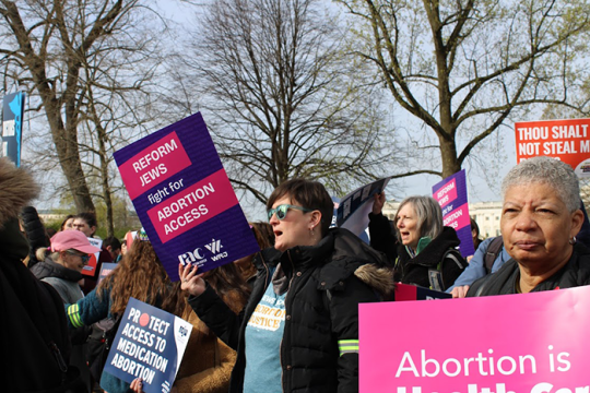 Photo of an abormation rally; one woman holding a sign that says "Reform Jews fight for abortoin access"