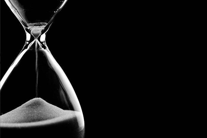 Clear hourglass with white sand against a stark black background