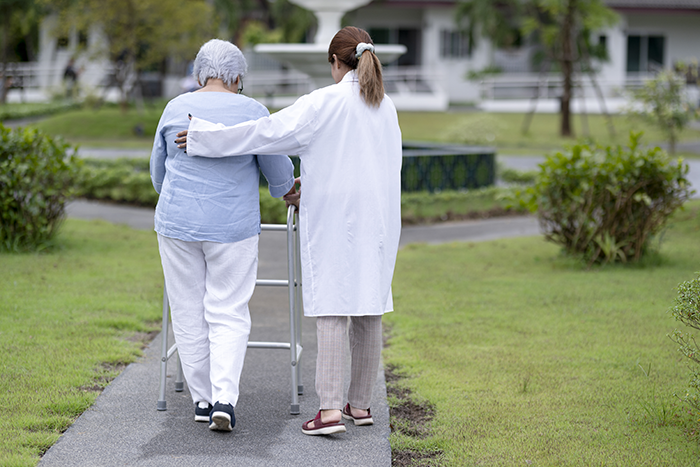 Female staff caring for elderly women in nursing homes, senior women using walking aids, nurses caring for the elderly while exercising, rear view.