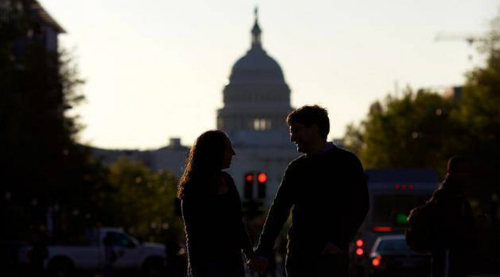 Happy couple holding hands in front of the silhouette of the US Capitol building 