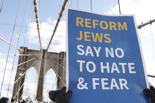 hands holding sign in front of Brooklyn Bridge saying Reform Jews Say No to Hate and Fear