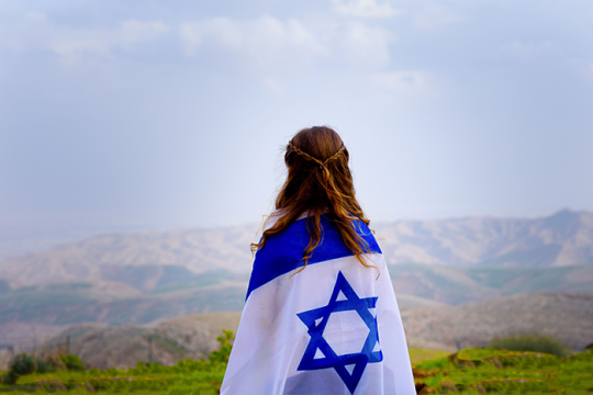 an image of an Israeli flag wrapped around a girl overlooking hills in Israel